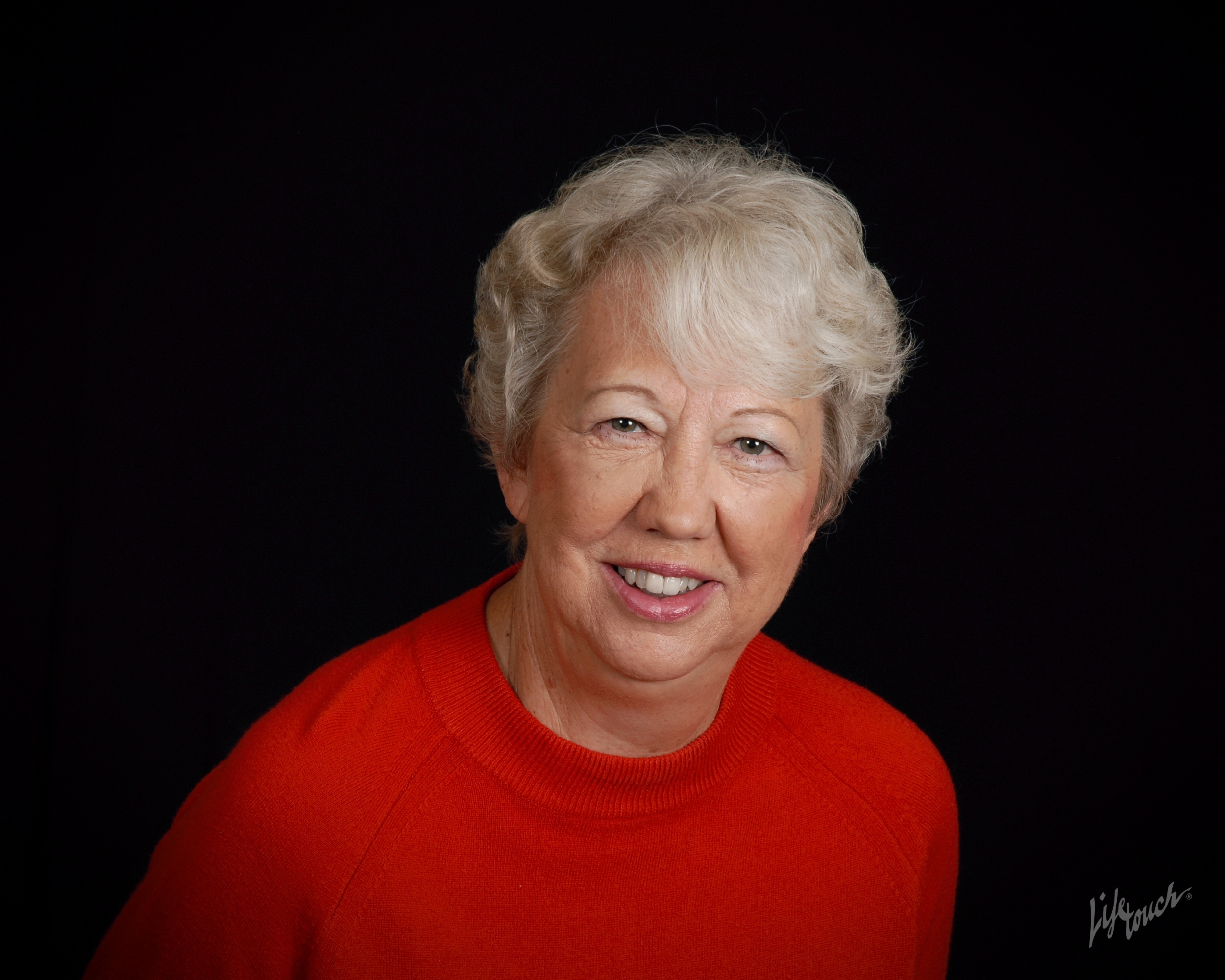 White haired lady in a red shirt on a black background