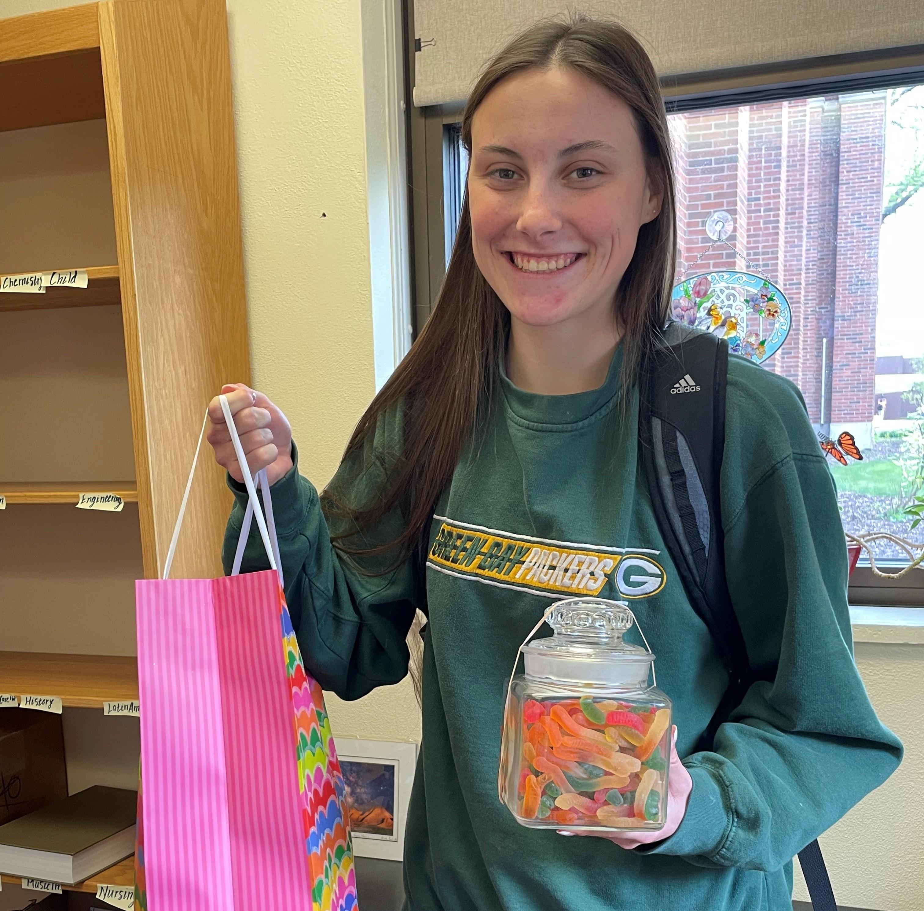 Photo of a young woman holding a gift bag and a glass jar of colorful gummy worms.