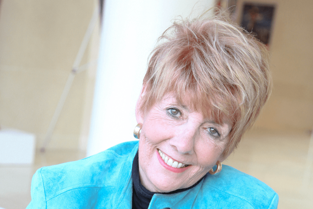 White woman with short blonde hair and a blue jacket smiling at the camera.
