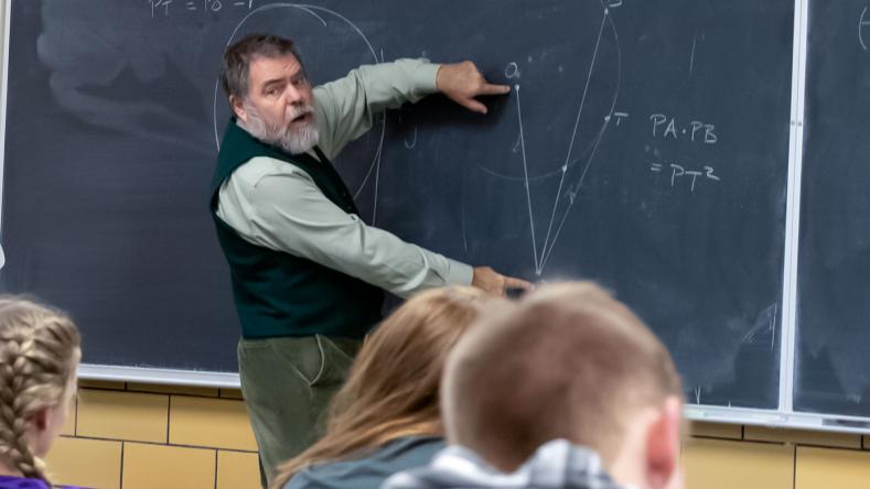 Professor at chalkboard reviewing problem